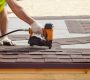 Construction worker putting the asphalt roofing (shingles) with nail gun on a new frame house