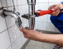 Male Plumber's Hand Repairing Sink Pipe Leakage With Adjustable Wrench