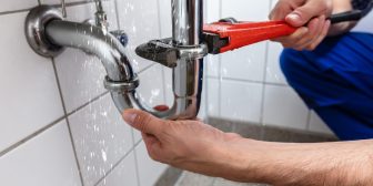 Male Plumber's Hand Repairing Sink Pipe Leakage With Adjustable Wrench