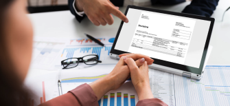 A man and a woman are sitting across the table from each other. The man is presenting an invoice to the woman on an ipad.