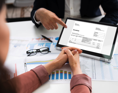 A man and a woman are sitting across the table from each other. The man is presenting an invoice to the woman on an ipad.
