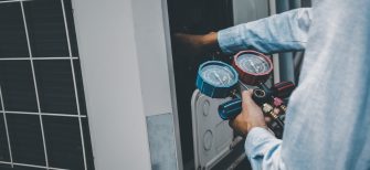 Air repair mechanic using measuring equipment for filling industrial factory air conditioners and checking maintenance outdoor air compressor unit.