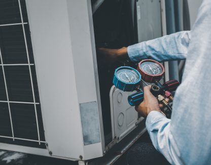 Air repair mechanic using measuring equipment for filling industrial factory air conditioners and checking maintenance outdoor air compressor unit.