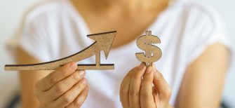 Closeup of woman hand holding wooden dollar sign and line and arrow sign.