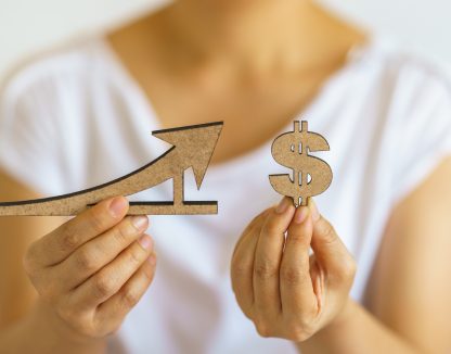 Closeup of woman hand holding wooden dollar sign and line and arrow sign.