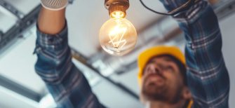 electrician working in a garage, installing light bulb electrician fixing electricity change skilled expert professional repair adult ceiling LED electric working renovation expert work DIY ladder expertise smiling support