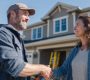 A contractor and homeowner shake hands outside a renovated home.