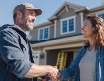 A contractor and homeowner shake hands outside a renovated home.