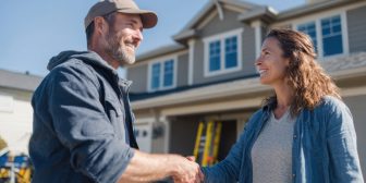A contractor and homeowner shake hands outside a renovated home.