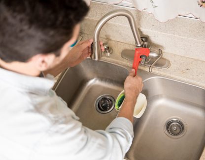 Male plumber using a wrench to tighten a water faucet in a kitchen, seen up close