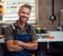 A plumber smiling in a kitchen in front of a sink