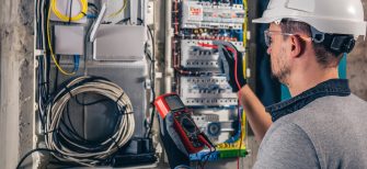 Man, an electrical technician working in a switchboard with fuses. Installation and connection of electrical equipment. Professional uses a tablet.