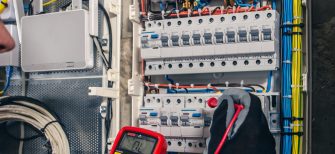 Man, an electrical technician working in a switchboard with fuses. Installation and connection of electrical equipment. Professional uses a tablet.