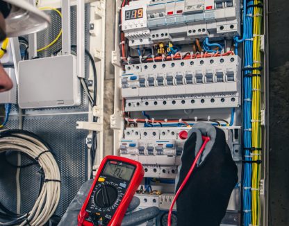 Man, an electrical technician working in a switchboard with fuses. Installation and connection of electrical equipment. Professional uses a tablet.