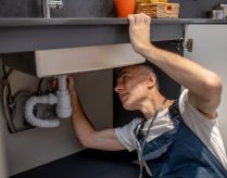 Plumber, repair. Experienced attentive middle-aged man carefully examining bottom of kitchen sink touching pipe with his hand diagnosing problem SSUCv3H4sIAAAAAAAACnRSQU7DMBC8I/GHyOdGSuskJf0BBwT3isPG3ramrl3ZThGq+DvrOEY+wC07szs748398aGq2AheCbar7rGiWmk9+eAgKGsIblYL7tBIdCVyc7xvSgClCtYp0CU4QhAnAxck0ExaR/h7JpkPECaPPm5fIAEBj6SRwF+JZHGf6ioTM0kTRLFnE9Ap6zxbFaSfxki+jh8ogmeZScv+UXpDe9X4l8yL8gK1BoN2KsTSx3sODEc04mvOVGR1qBFS1n1qZedPsnwp08MklS2C36wAHRt4oXR1SihzLMZsOM2XyWPCTia4aIHlGExbe4WRcu2qA2lixk/gPbXLjBeLBP0H9lLsMTbMARZVJulYsVzzzRMf+NB3XbvhfbtdLw3pwCdFOrOdLES1OCtZRlfRAdvIrYRDu61F0/O6HUHUwwBQd13Hh0PT4yg5Pfz3DwAAAP//AwCsHV1xuwIAAA==