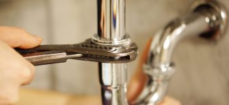 Plumbing repair service. Professional installer with spanner checking pipe.