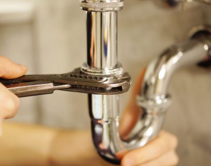 Plumbing repair service. Professional installer with spanner checking pipe.