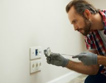 Portrait of electrician wearing protective gloves, using a screwdriver while installing new plug socket in a house. Electrical maintenance, repair service concept SSUCv3H4sIAAAAAAAEAH2Rz04DIRDG7ya+w4ZzN1lbKru+g9F742GAsYul0PBH0zR9d2EpysF4Y37fzAcfc7m/6zrCwStBnrpLrlKttI4+OAjKmoSH1Y07NBJdS1CqYJ0C3UIOQcwGjpigiVpnfF1E4gOE6NHny25IQMB98ijwx6K8aFfqrgqLmCaSRF7RnjSSVaP4yLPyjIZUel39Y/HCP1AE/6eH8gK1BoM2+l+3cnirUWGPRpyXNE1KhxqhpNyVVnL4CuiObW6IUtkm8qcVoHPDpnE6OSWU2TdjNszLCuqYsNEEl59AagyirT0B1/n/35MnVj6D96ldVt5cJNLC7bG5x9iwBLi5EpnWlMuHzXq7ptM4PI7baZzYSEldrRUHJduIZduzSpI7N1zlFxBKx4kDoz1bA+upHFjPcQv9o2AIfKI4MJk+/voN5K/JfaQCAAA=