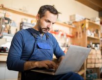 Portrait of mature worker using laptop in carpenters workshop interior, copy space