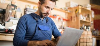 Portrait of mature worker using laptop in carpenters workshop interior, copy space