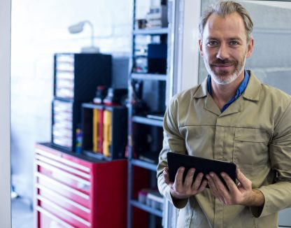 Portrait of smiling mechanic using digital tablet in repair shop