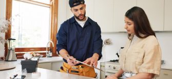 Woman, home and plumber with contract on clipboard for maintenance service, information and repairs. Kitchen, discussion and man with notes in checklist for renovation, inspection or customer invoice.