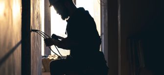 A construction electrician cuts a voltage cable during a repair, silhouette in the light of the setting sun.