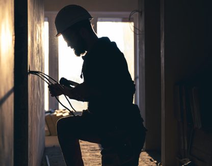 A construction electrician cuts a voltage cable during a repair, silhouette in the light of the setting sun.