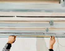 Worker's hands measure and adjust a metal profile for mounting a plasterboard ceiling frame, close-up, selective focus in the hands of a specialist. Industrial renovation and renovation