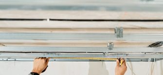 Worker's hands measure and adjust a metal profile for mounting a plasterboard ceiling frame, close-up, selective focus in the hands of a specialist. Industrial renovation and renovation
