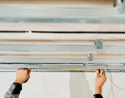 Worker's hands measure and adjust a metal profile for mounting a plasterboard ceiling frame, close-up, selective focus in the hands of a specialist. Industrial renovation and renovation
